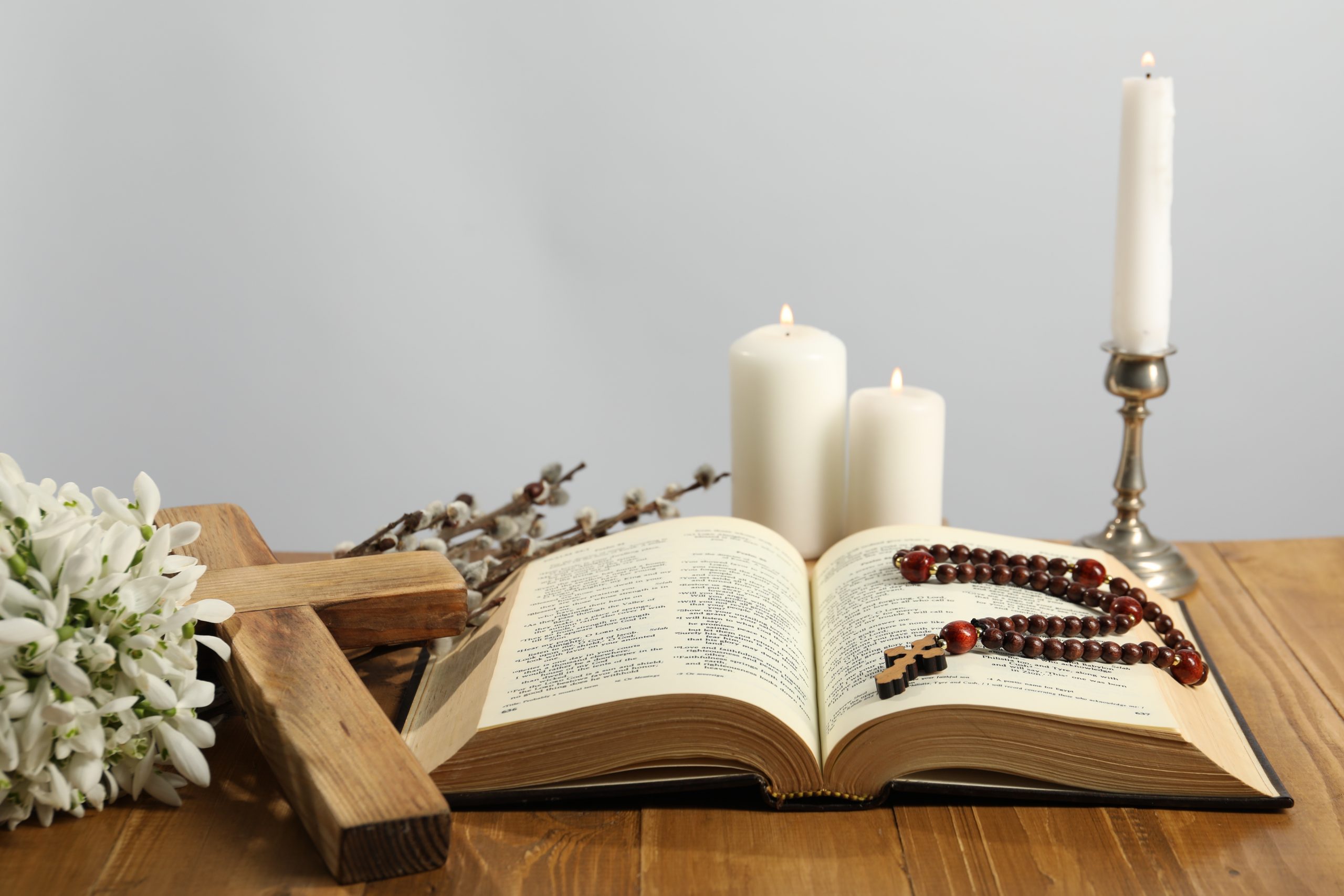 Church candles, cross, rosary beads, Bible, snowdrops and willow branches on wooden table against light background
